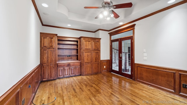 interior space with ceiling fan, a raised ceiling, crown molding, light wood-type flooring, and french doors