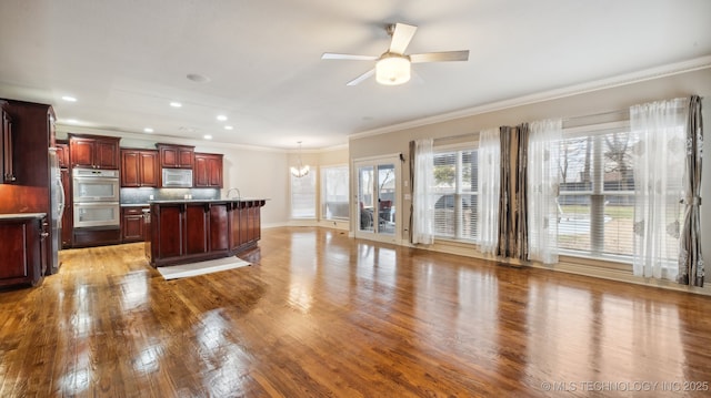 kitchen with appliances with stainless steel finishes, tasteful backsplash, wood-type flooring, ornamental molding, and a center island with sink