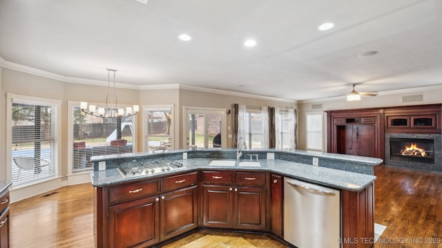 kitchen with sink, stone countertops, hanging light fixtures, appliances with stainless steel finishes, and an island with sink