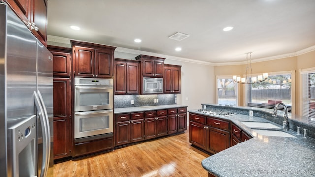 kitchen featuring tasteful backsplash, sink, hanging light fixtures, light hardwood / wood-style floors, and stainless steel appliances