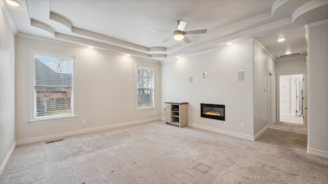 unfurnished living room featuring a raised ceiling, crown molding, light carpet, and ceiling fan