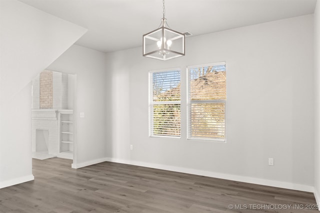 unfurnished dining area with a brick fireplace, dark wood-type flooring, and an inviting chandelier