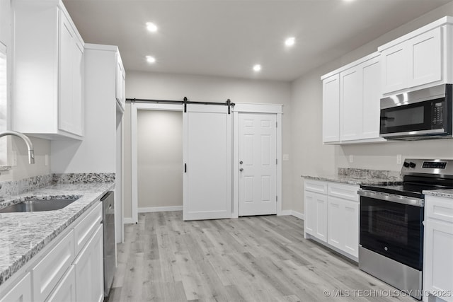 kitchen with sink, stainless steel appliances, a barn door, light stone countertops, and white cabinets