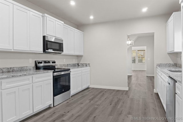 kitchen with stainless steel appliances, white cabinetry, light stone countertops, and light wood-type flooring