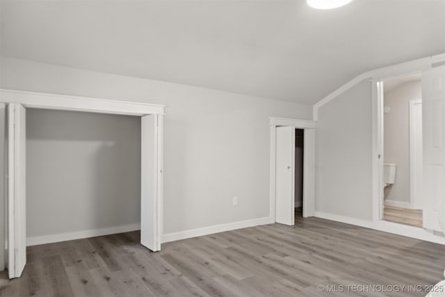 unfurnished bedroom with multiple closets, lofted ceiling, and light hardwood / wood-style floors