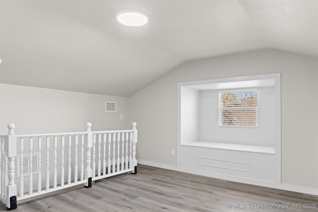 additional living space with vaulted ceiling, light hardwood / wood-style floors, and a textured ceiling