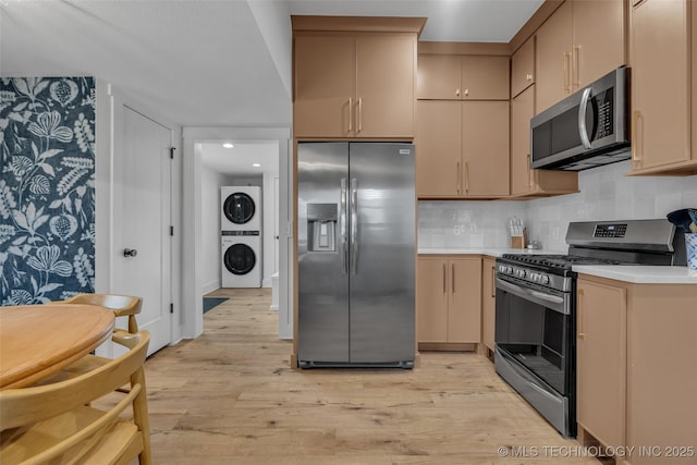 kitchen featuring light brown cabinets, light wood-type flooring, stainless steel appliances, and stacked washer / dryer