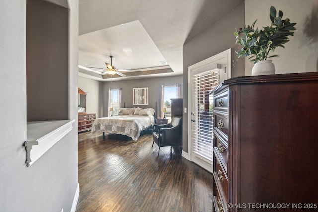 bedroom with dark wood-type flooring, access to outside, ceiling fan, and a tray ceiling