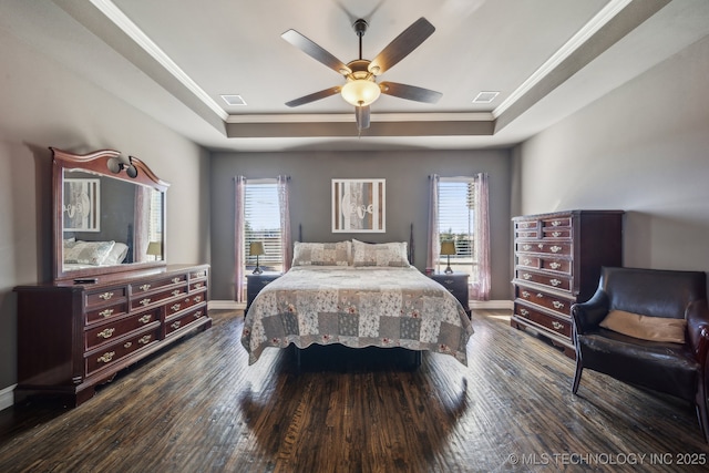 bedroom with a raised ceiling, dark wood-type flooring, and multiple windows