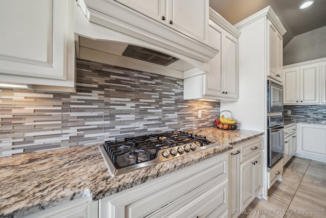 kitchen with premium range hood, white cabinetry, backsplash, light stone counters, and stainless steel appliances