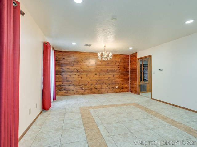 spare room featuring a chandelier, light tile patterned floors, a textured ceiling, and wood walls