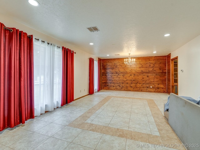 tiled spare room featuring wooden walls, a textured ceiling, and a notable chandelier