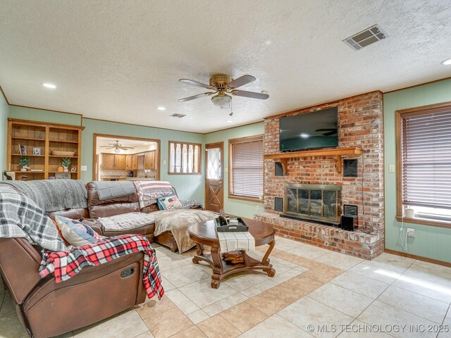 living room featuring ceiling fan, a brick fireplace, light tile patterned floors, and a textured ceiling