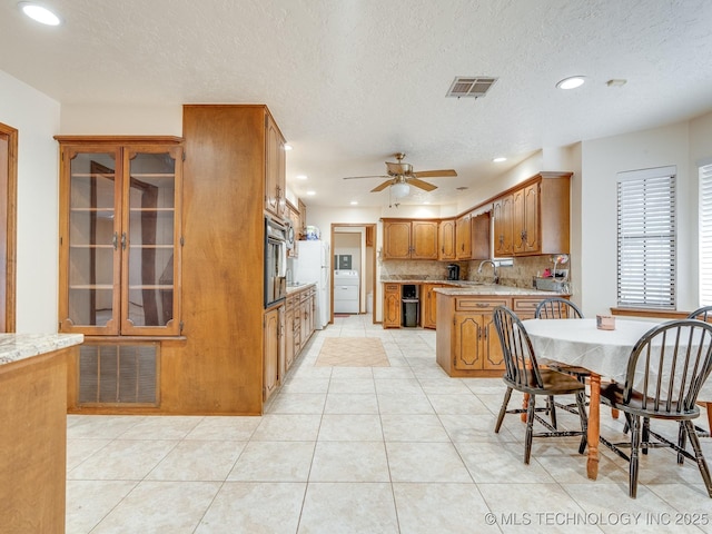 kitchen featuring light tile patterned flooring, tasteful backsplash, washer / clothes dryer, sink, and oven