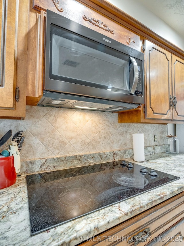 interior details with light stone counters, black electric stovetop, and backsplash