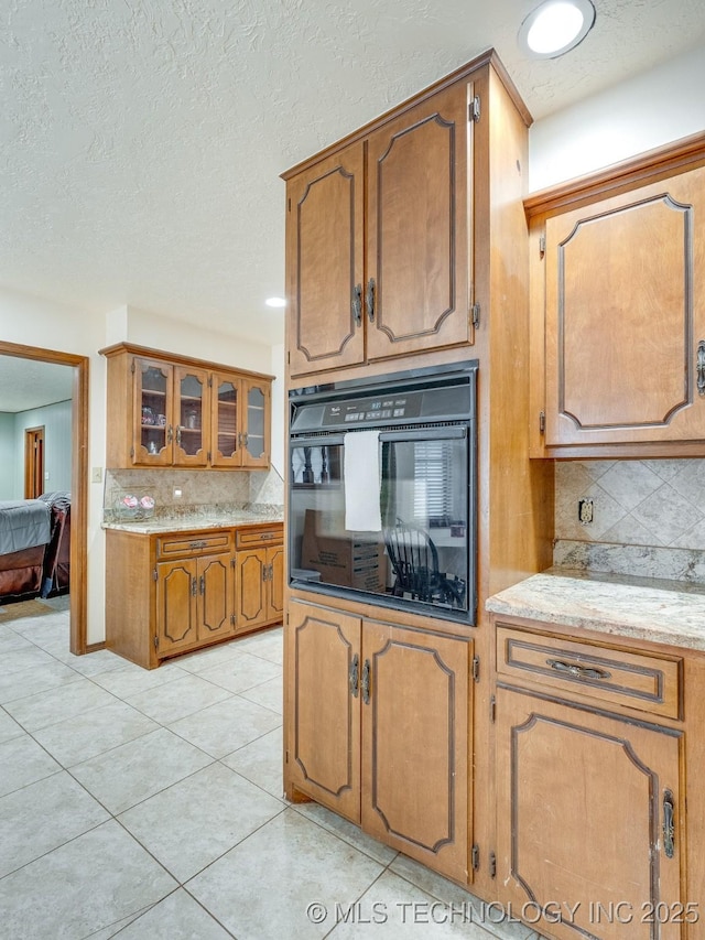 kitchen with tasteful backsplash, light tile patterned floors, black oven, and a textured ceiling