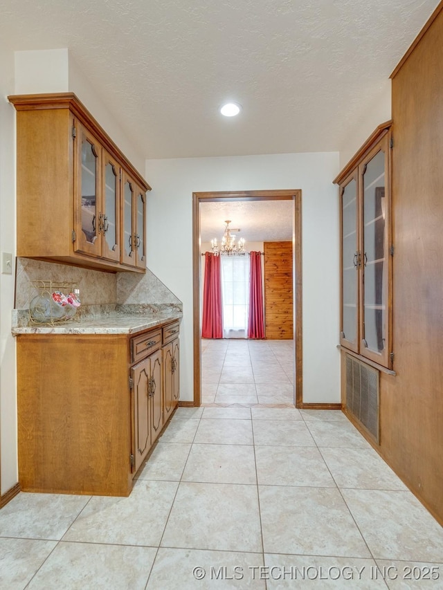 kitchen with a notable chandelier, light stone countertops, a textured ceiling, light tile patterned flooring, and decorative backsplash