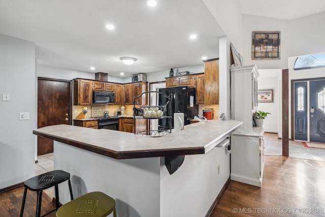 kitchen with backsplash, kitchen peninsula, a breakfast bar area, and black appliances