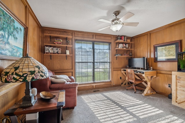 carpeted office featuring built in shelves, ceiling fan, and wood walls