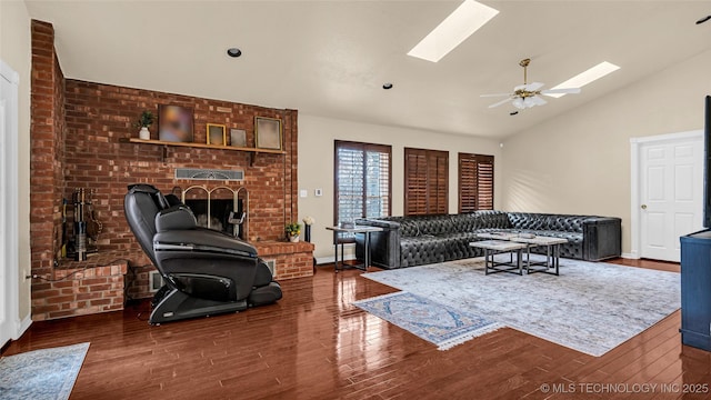 living room with ceiling fan, vaulted ceiling with skylight, dark hardwood / wood-style flooring, and a brick fireplace