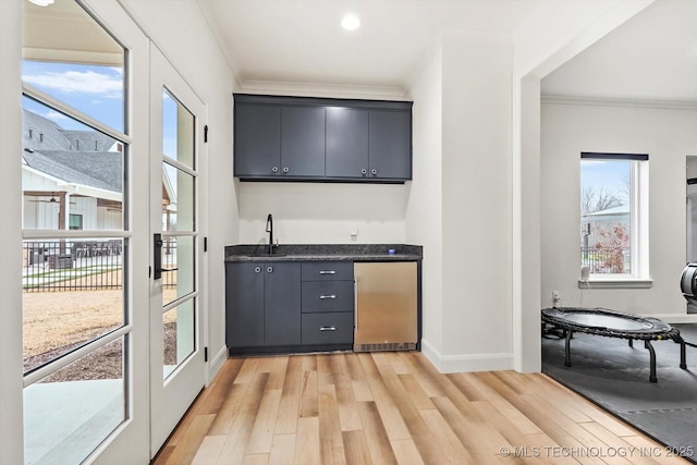 bar with ornamental molding, light hardwood / wood-style flooring, fridge, and sink