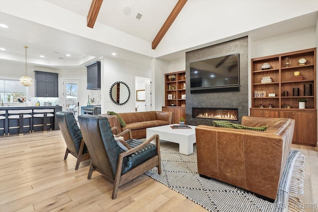 living room with vaulted ceiling with beams, light hardwood / wood-style flooring, a large fireplace, and a raised ceiling