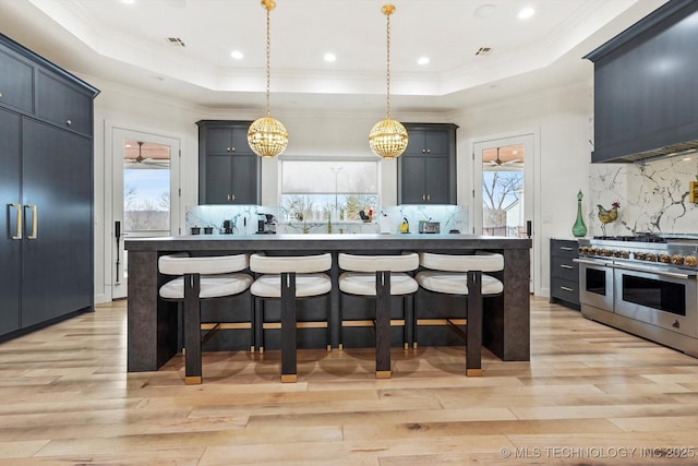 kitchen featuring double oven range, pendant lighting, a breakfast bar area, and a tray ceiling