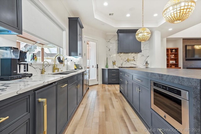 kitchen featuring sink, crown molding, light hardwood / wood-style flooring, decorative light fixtures, and a raised ceiling