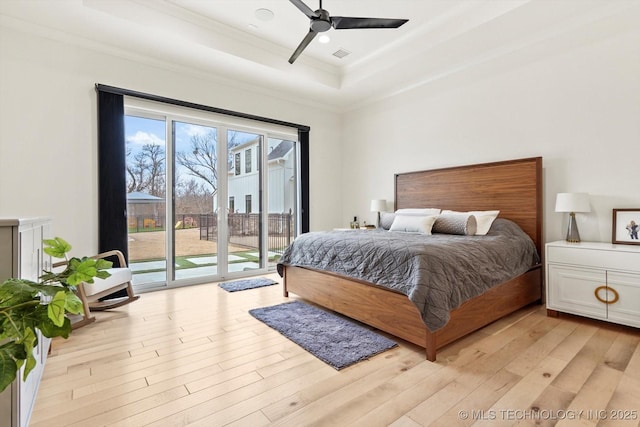 bedroom featuring ornamental molding, access to exterior, ceiling fan, a tray ceiling, and light wood-type flooring