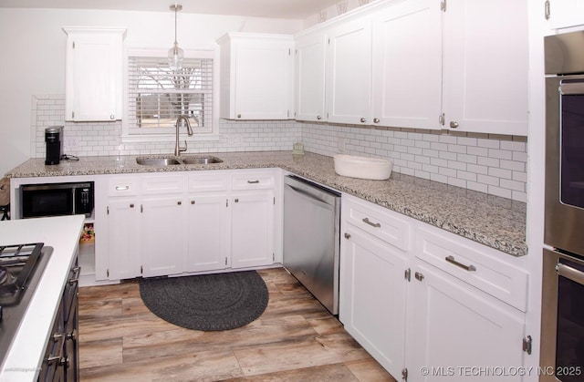 kitchen with sink, stainless steel appliances, light stone counters, white cabinets, and decorative light fixtures