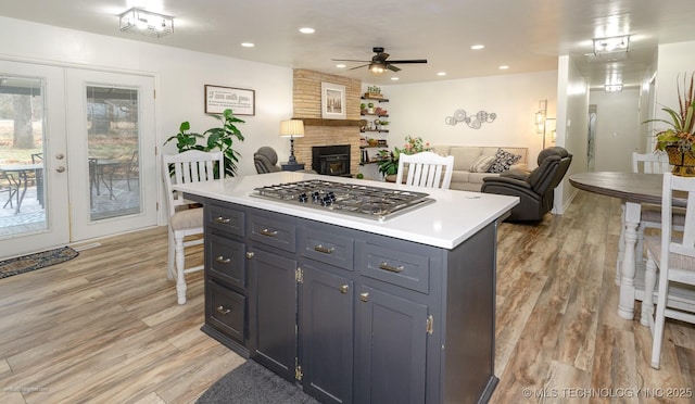 kitchen featuring a fireplace, a center island, stainless steel gas cooktop, light wood-type flooring, and french doors