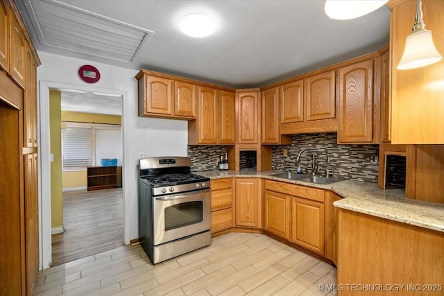 kitchen featuring sink, gas stove, decorative light fixtures, light stone countertops, and backsplash