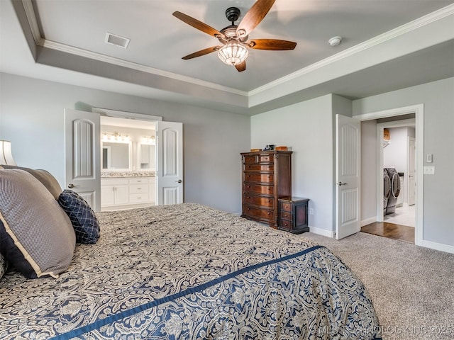 carpeted bedroom featuring independent washer and dryer, connected bathroom, ornamental molding, a tray ceiling, and ceiling fan