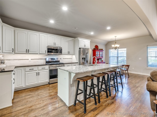 kitchen with a breakfast bar, appliances with stainless steel finishes, white cabinetry, a center island with sink, and decorative light fixtures