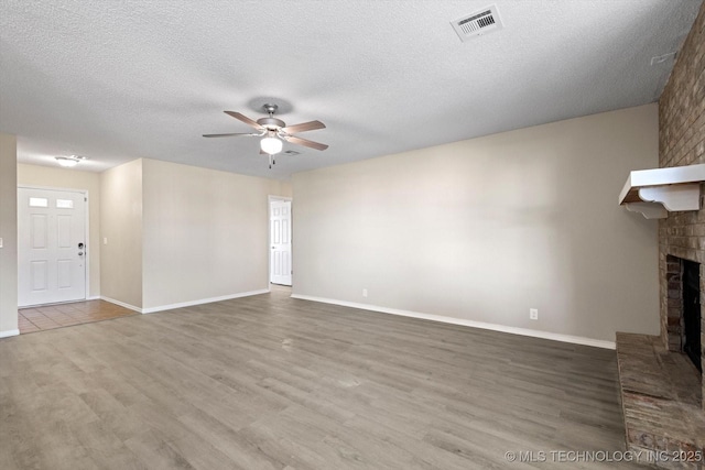 unfurnished living room with hardwood / wood-style flooring, ceiling fan, a fireplace, and a textured ceiling