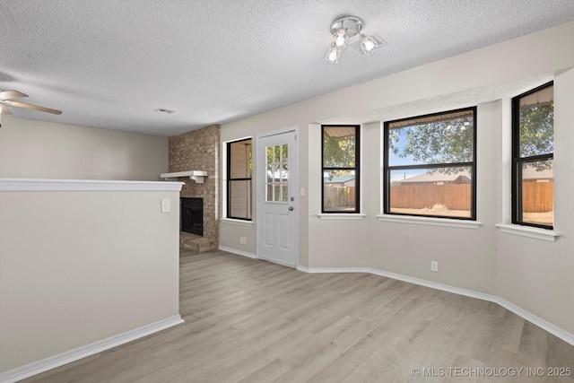 spare room featuring ceiling fan, a brick fireplace, a textured ceiling, and light wood-type flooring