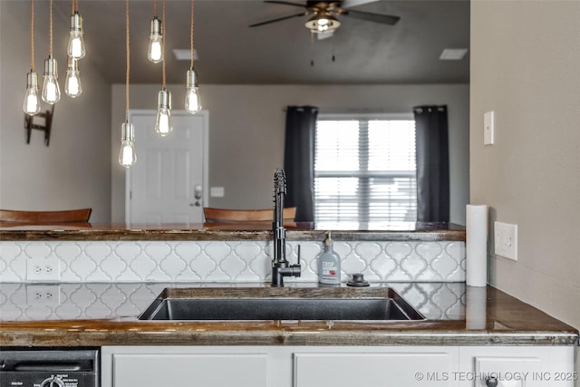 kitchen with sink, white cabinetry, decorative light fixtures, dishwashing machine, and backsplash