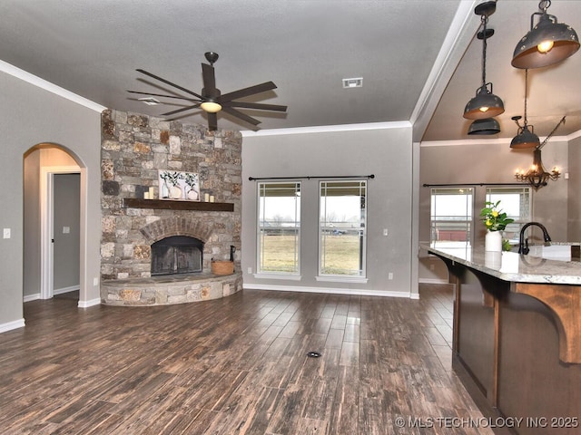 living room featuring a stone fireplace, sink, dark hardwood / wood-style flooring, ornamental molding, and ceiling fan