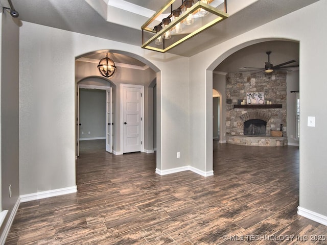 empty room featuring dark wood-type flooring, ceiling fan, and a stone fireplace