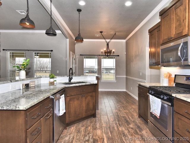 kitchen with sink, crown molding, appliances with stainless steel finishes, hanging light fixtures, and light stone counters