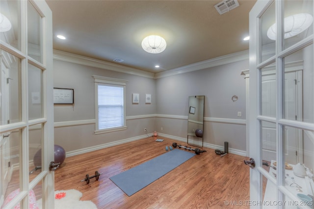 exercise area featuring wood-type flooring, ornamental molding, and french doors