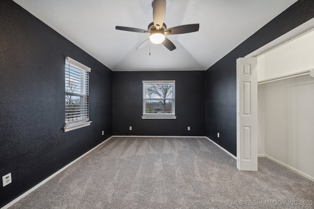 unfurnished bedroom featuring multiple windows, vaulted ceiling, carpet flooring, and ceiling fan