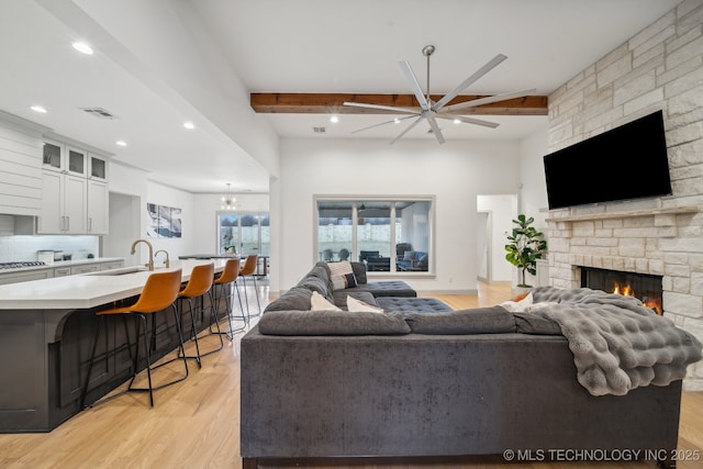 living room featuring sink, ceiling fan, a fireplace, light hardwood / wood-style floors, and beamed ceiling