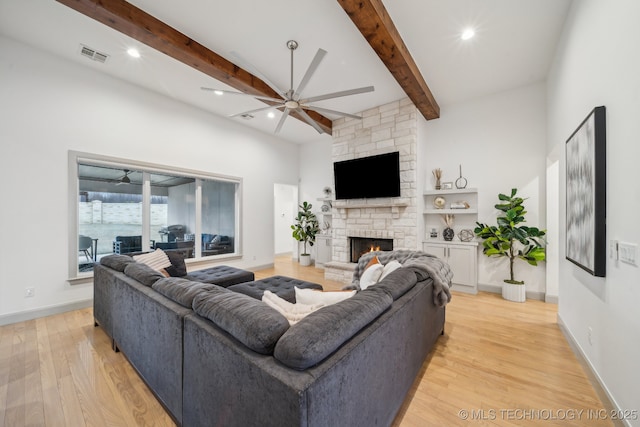 living room featuring beam ceiling, a stone fireplace, light hardwood / wood-style floors, and ceiling fan