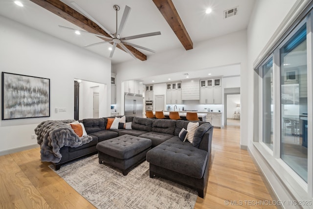 living room with beamed ceiling, ceiling fan, light hardwood / wood-style floors, and a high ceiling