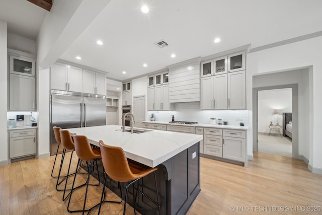 kitchen featuring appliances with stainless steel finishes, a breakfast bar area, light stone countertops, a center island with sink, and light hardwood / wood-style flooring