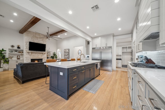 kitchen featuring custom exhaust hood, white cabinetry, light hardwood / wood-style flooring, appliances with stainless steel finishes, and an island with sink