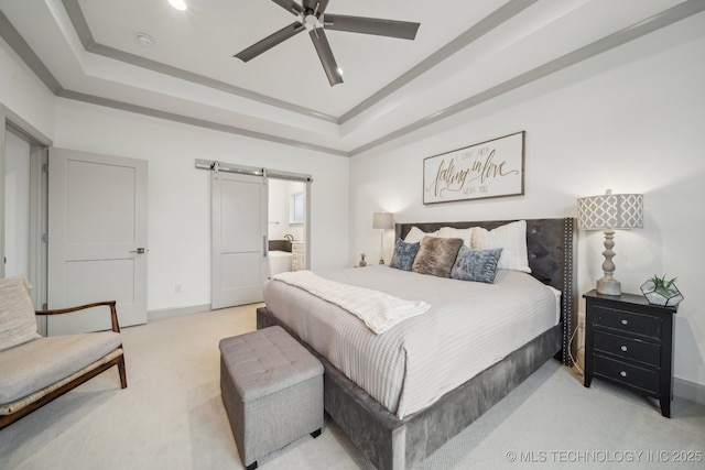 carpeted bedroom with ensuite bathroom, a barn door, ornamental molding, and a tray ceiling