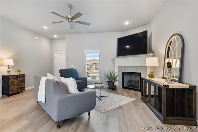 living room featuring ceiling fan, light hardwood / wood-style floors, and a tile fireplace