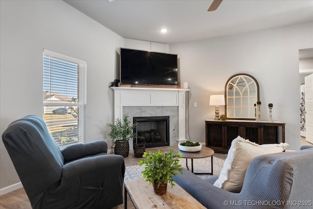 living room with wood-type flooring, a tile fireplace, and ceiling fan